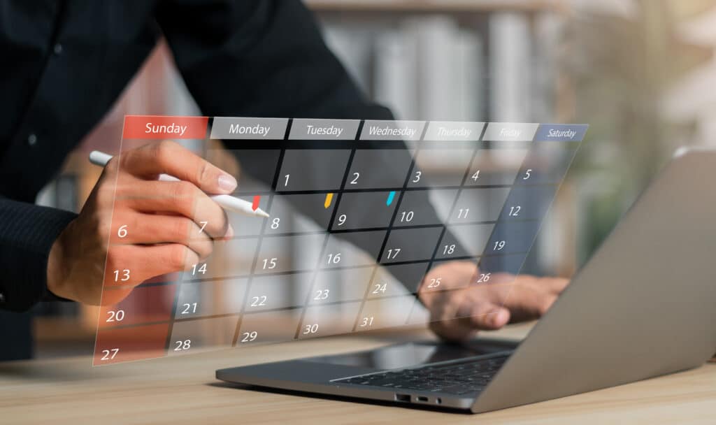 Imagem de um calendário em frente à um notebook com uma pessoa analisando as datas